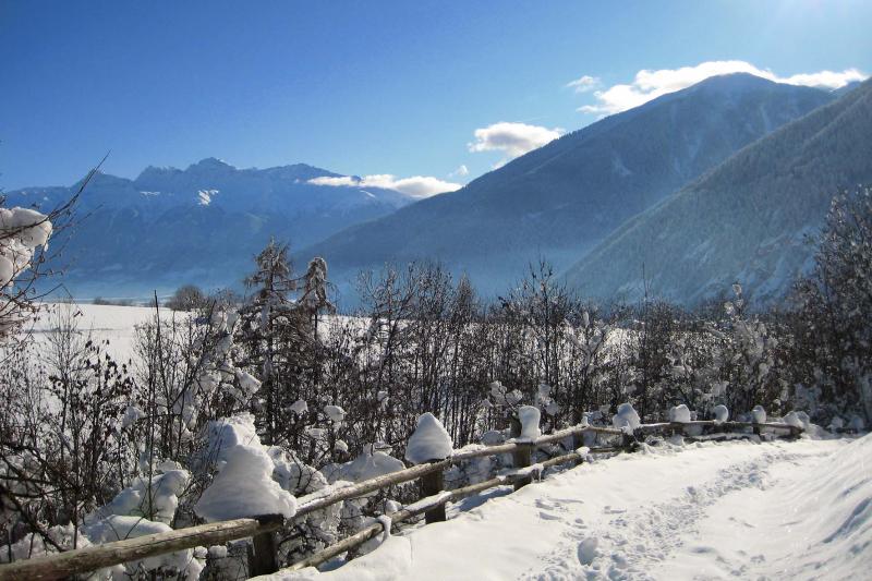 Verschneiter Weg mit Holzzaun in einer Berglandschaft